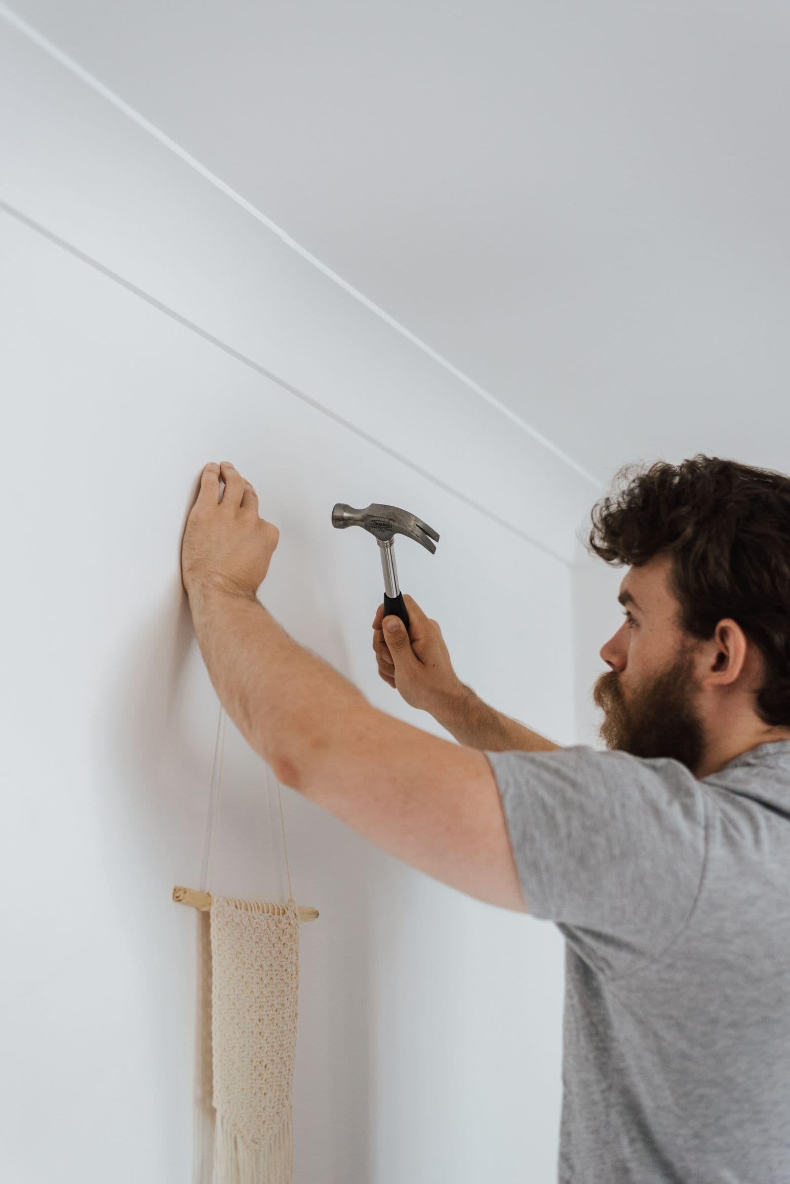 A handyman hammering a nail to hang wall decor inside a bright home